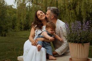 A couple shares a tender moment on a bench beside purple flowers in a lush garden setting at sunset.