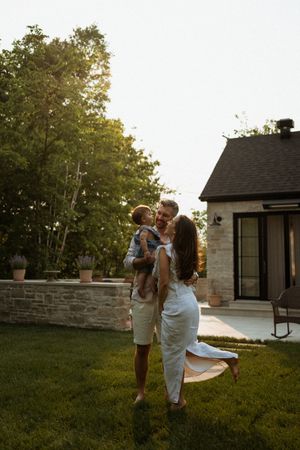A family shares a sunset moment together in their backyard with a stone wall and house in the background.