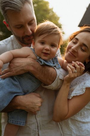 Candid sunset portrait of parents cuddling with their baby in matching light colored outfits.