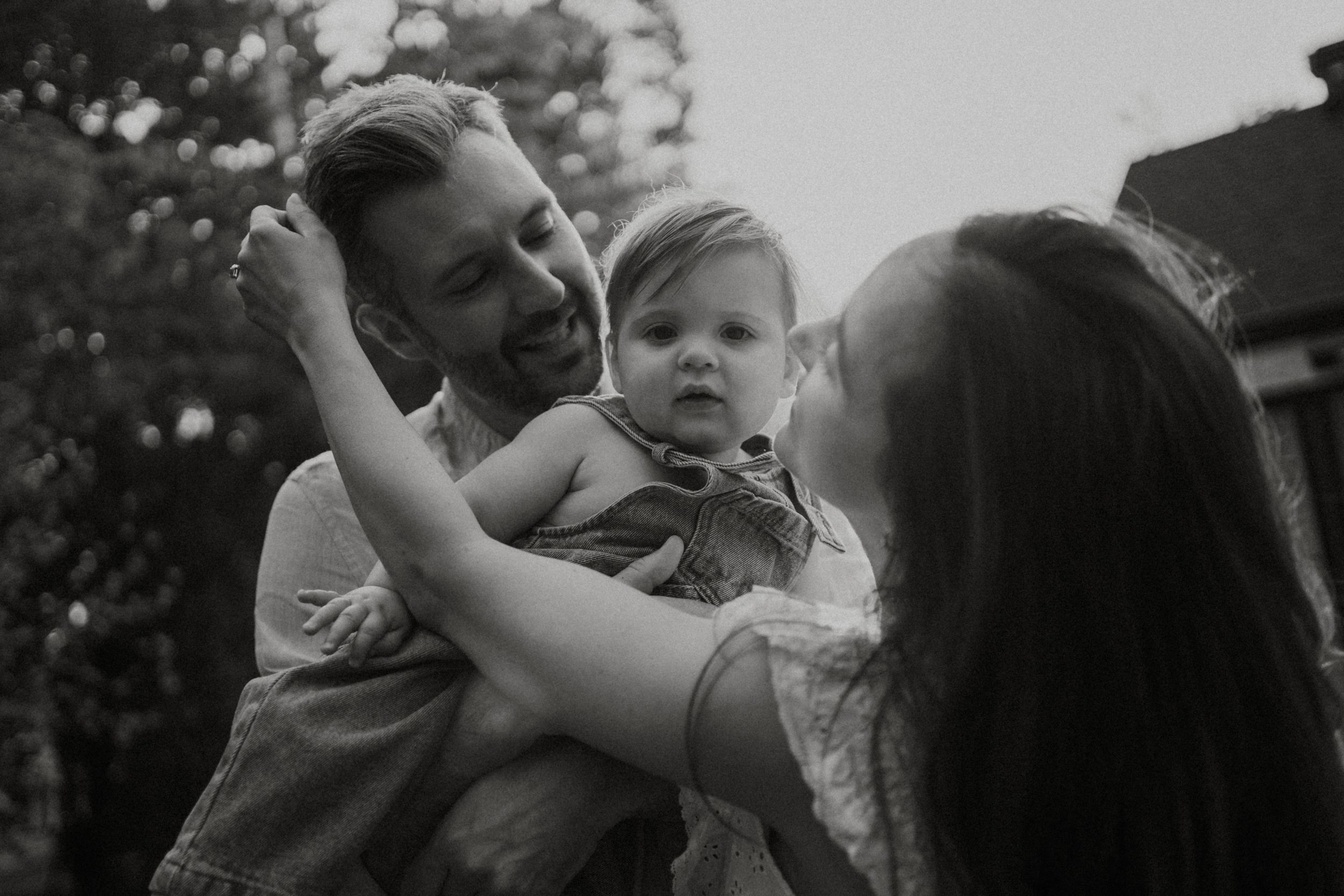 A joyful black and white photograph of a family sharing a playful moment together outdoors.
