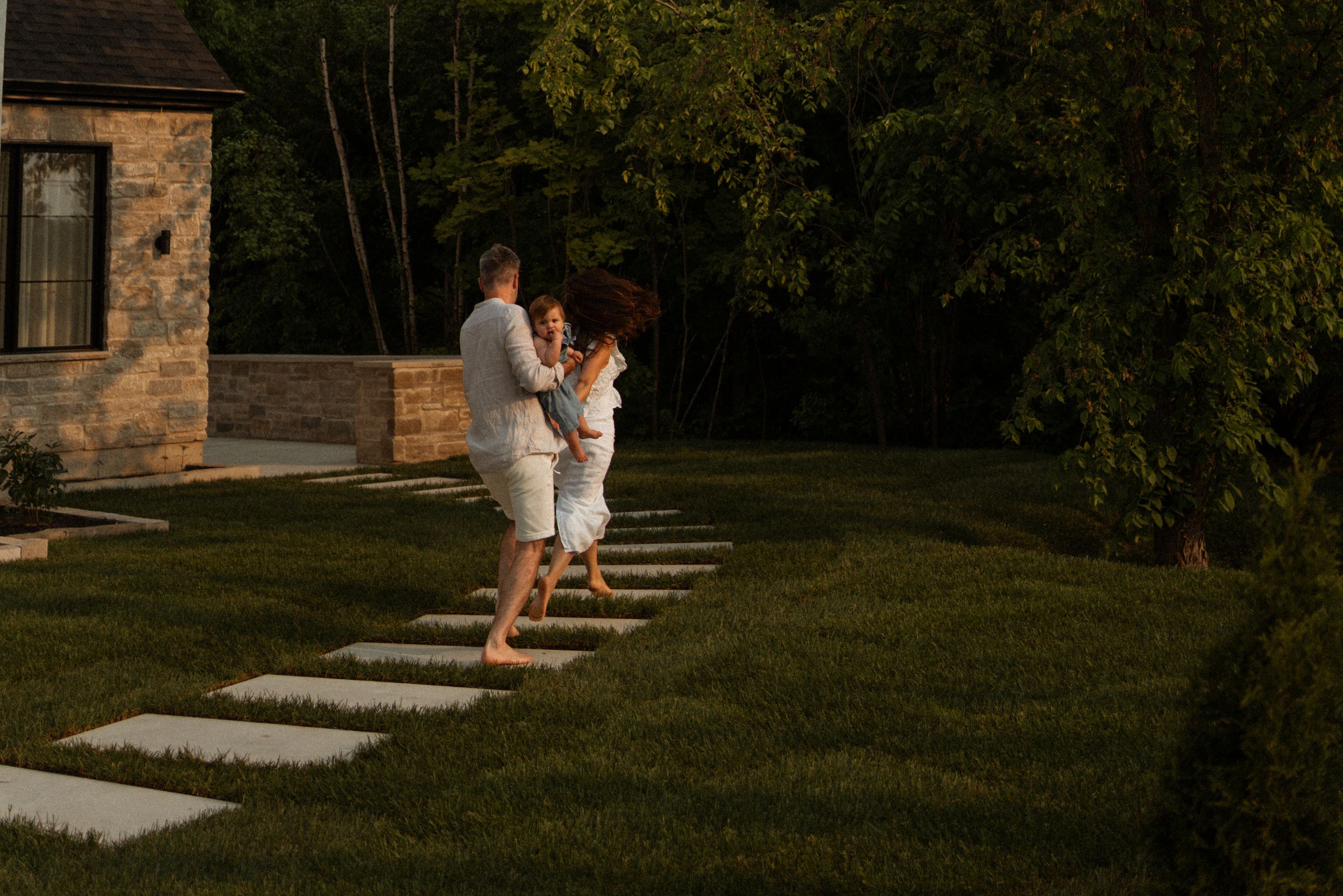 A couple shares a romantic moment at sunset on stone pathway steps leading through a green lawn beside a rustic building.