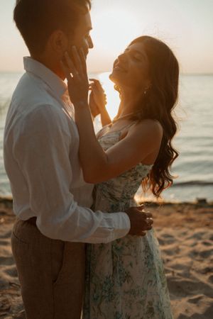 Romantic couple embraces on beach at sunset while sharing intimate moment together.