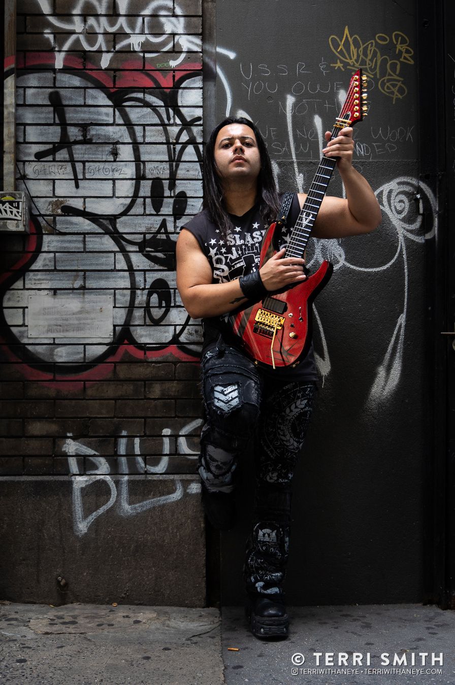 Luís (Luis) Kalil of Red Devil Vortex posed on a New York City street with graffiti background holding his custom ESP guitar