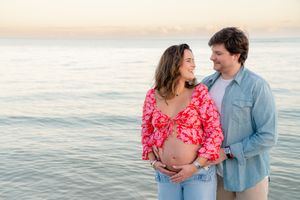 Couple shares tender moments during sunset beach photoshoot in coordinating red and blue outfits.