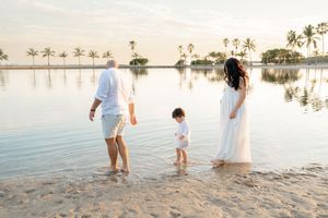 Family in white outfits walking along a tropical beach at sunset with palm trees in the background.