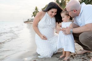 A family shares a tender moment together on a sandy beach at sunset wearing white clothing.
