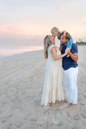 Family shares an intimate moment together on a sandy beach during sunset.