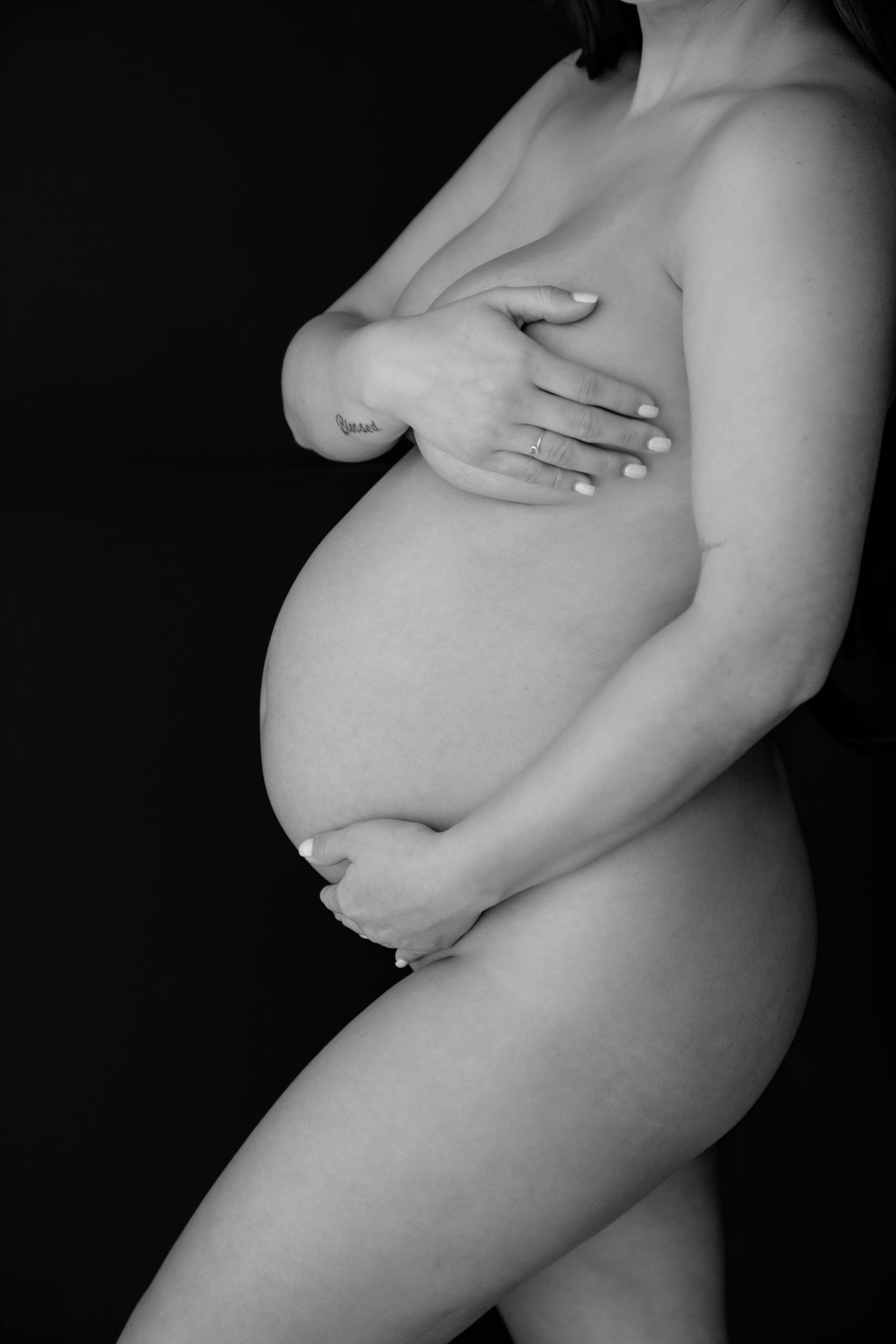 Black and white artistic nude maternity photos showing the side profile of a pregnant belly in dramatic lighting.