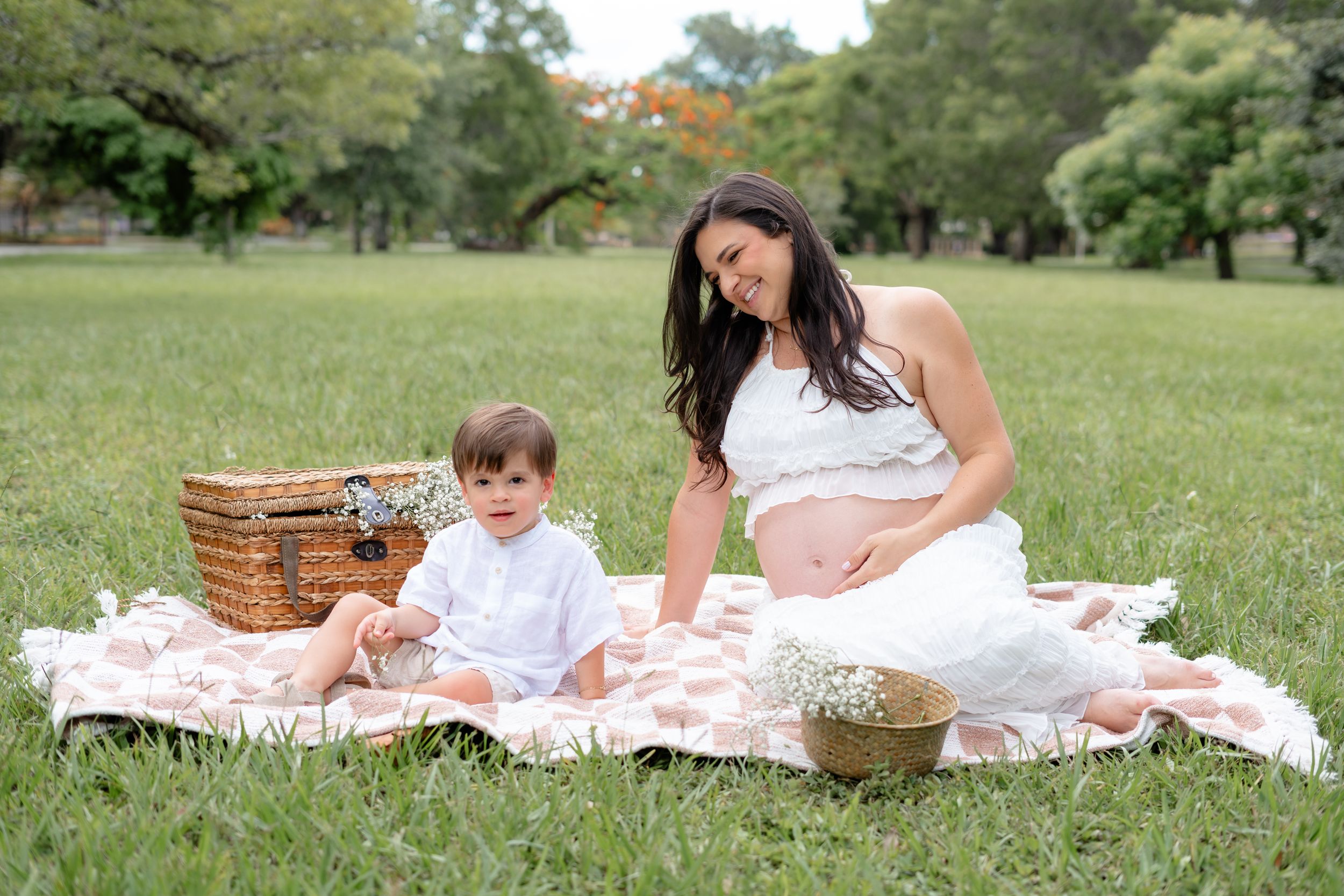 A family picnic scene on a white blanket in a grassy park with a woven basket nearby.