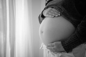 Black and white photo of hands gently cradling a pregnant belly against soft window light.