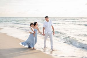 Three people walking along a sandy beach at sunset wearing white and blue outfits by the ocean waves.