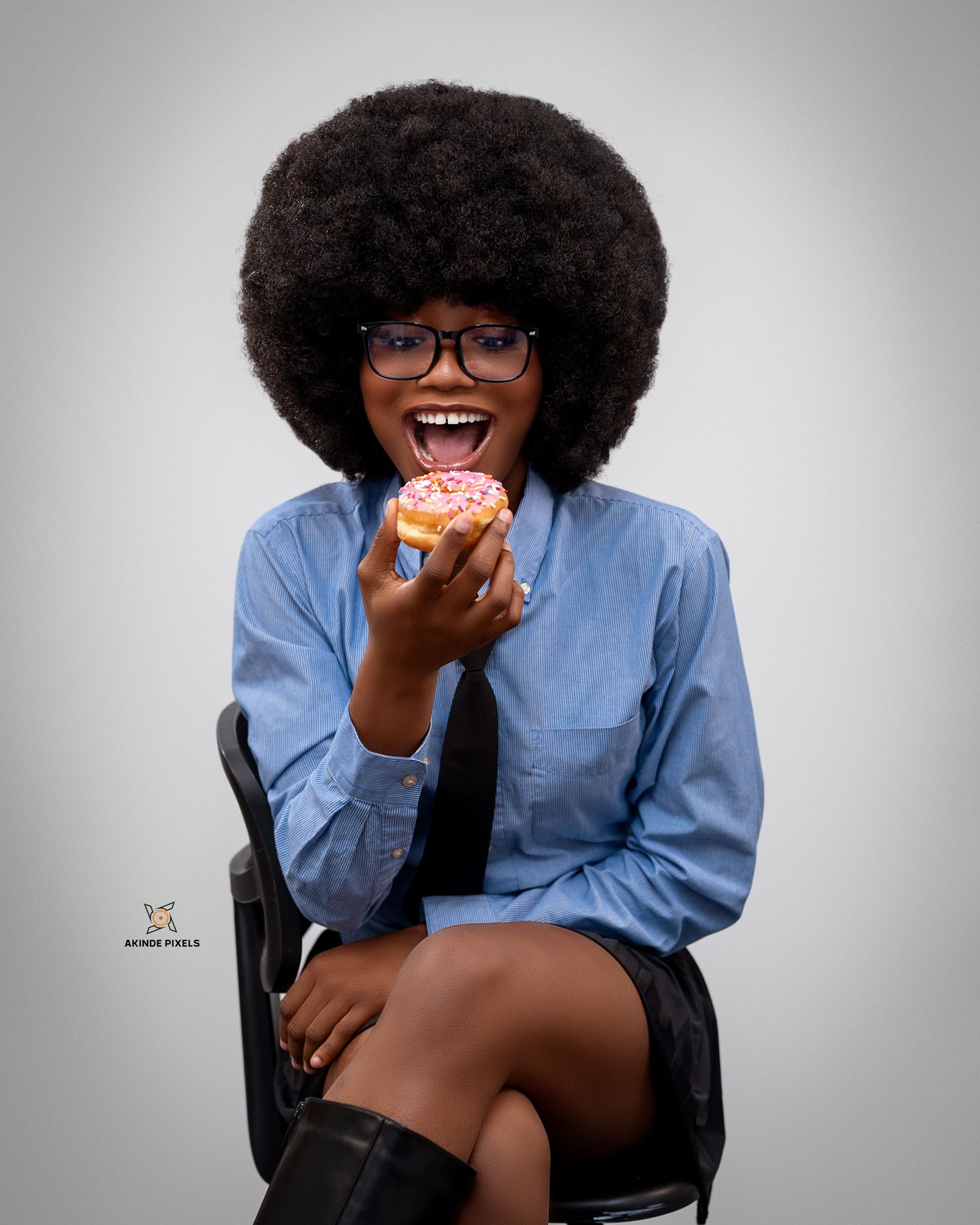Joyful studio portrait of a young woman with natural afro hairstyle, laughing while holding a colorful dunkin donut.