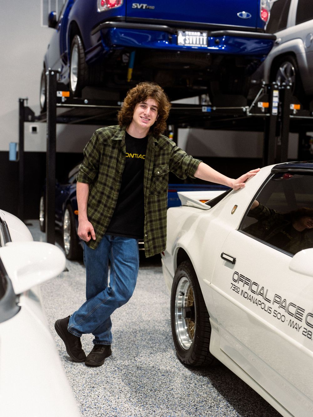 A collection of white Pontiac cars in a garage with a blue truck elevated on a hydraulic lift.