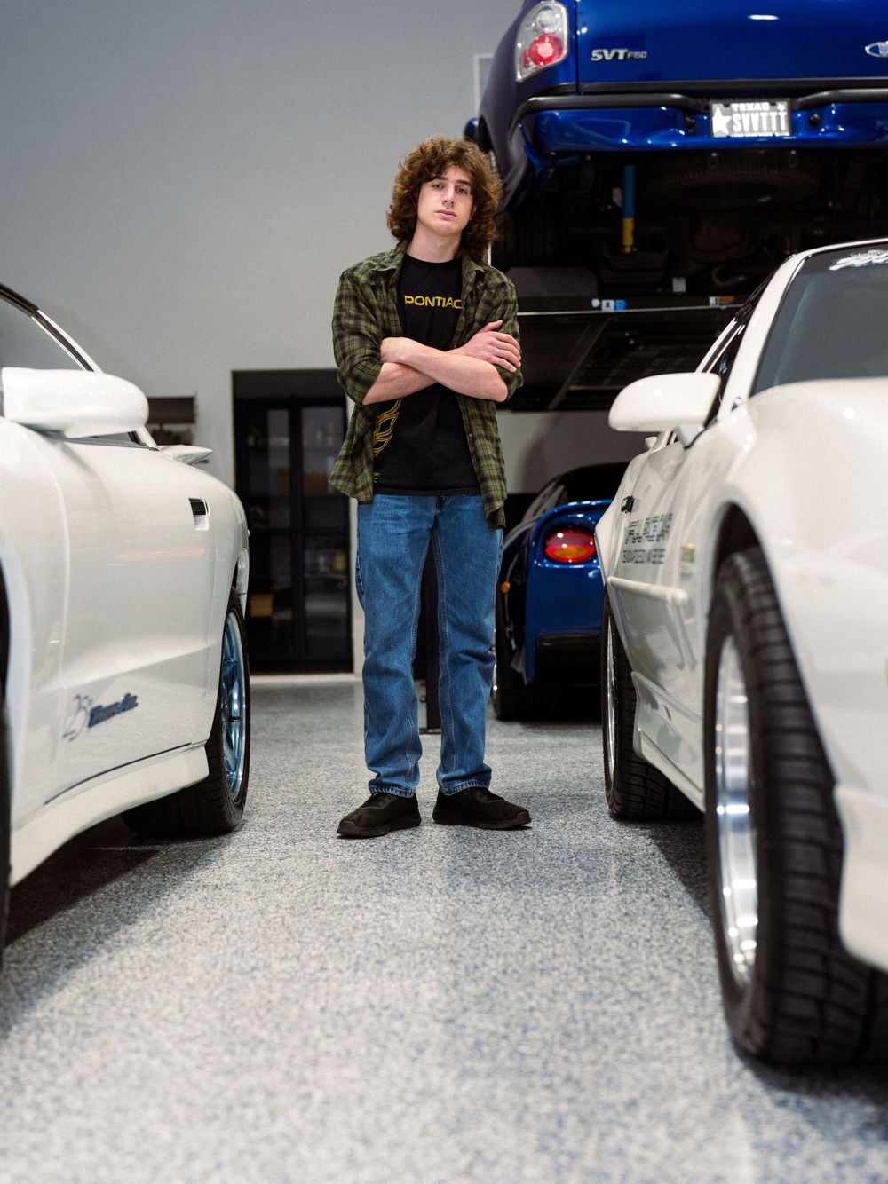 Car enthusiast standing between white Pontiac vehicles in an indoor garage space.