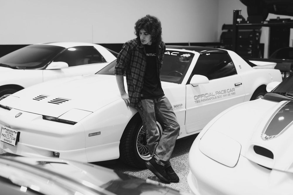Casual lifestyle portrait with classic white Pontiac Trans Am models in a garage setting.