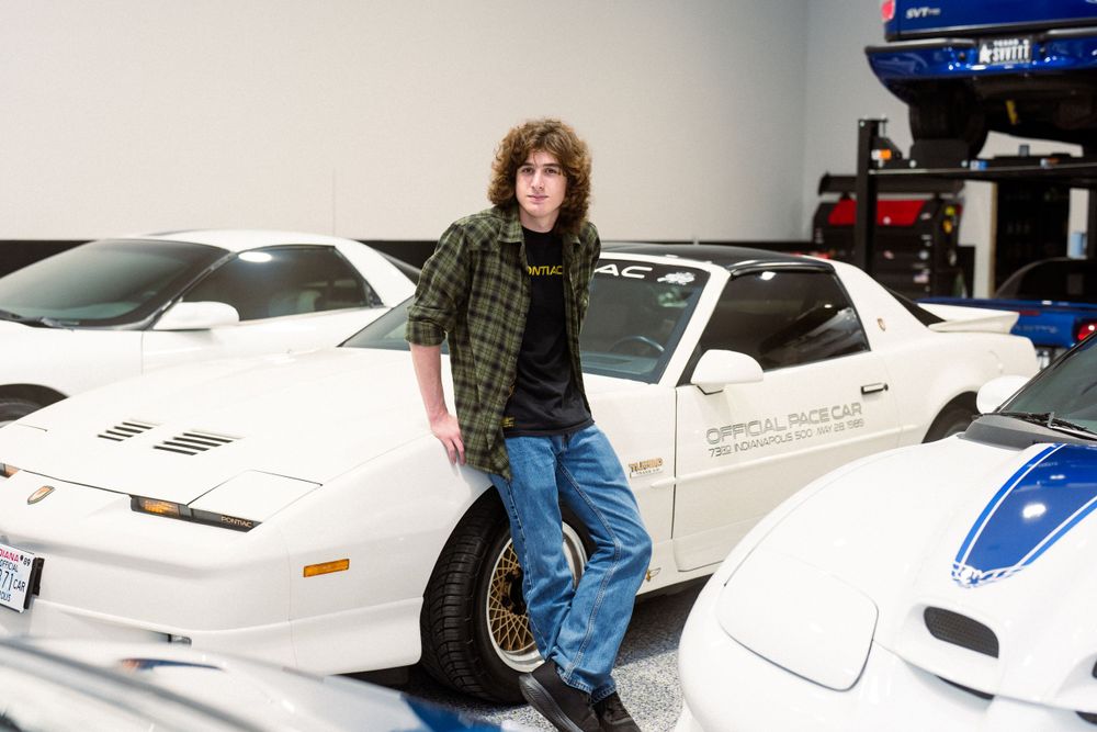 White Pontiac Trans Am displayed in a collector's garage with other classic vehicles.