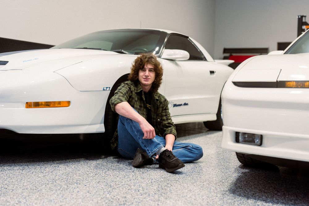 Person sitting between two white sports cars in a garage showroom.