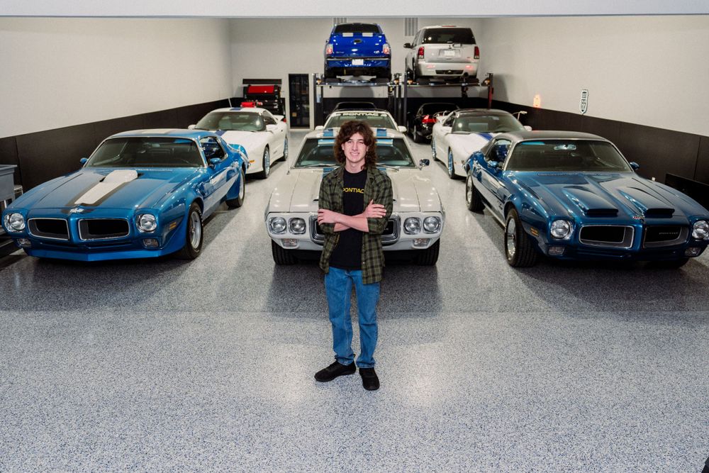 Person standing in garage with classic blue and silver Pontiac Trans Ams.