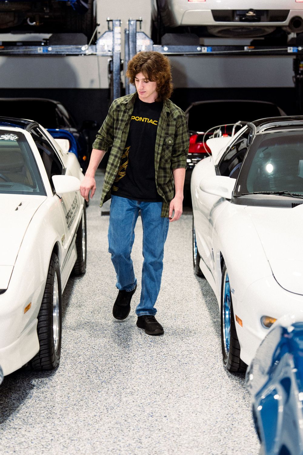 Person in plaid shirt walking between rows of white sports cars in showroom.