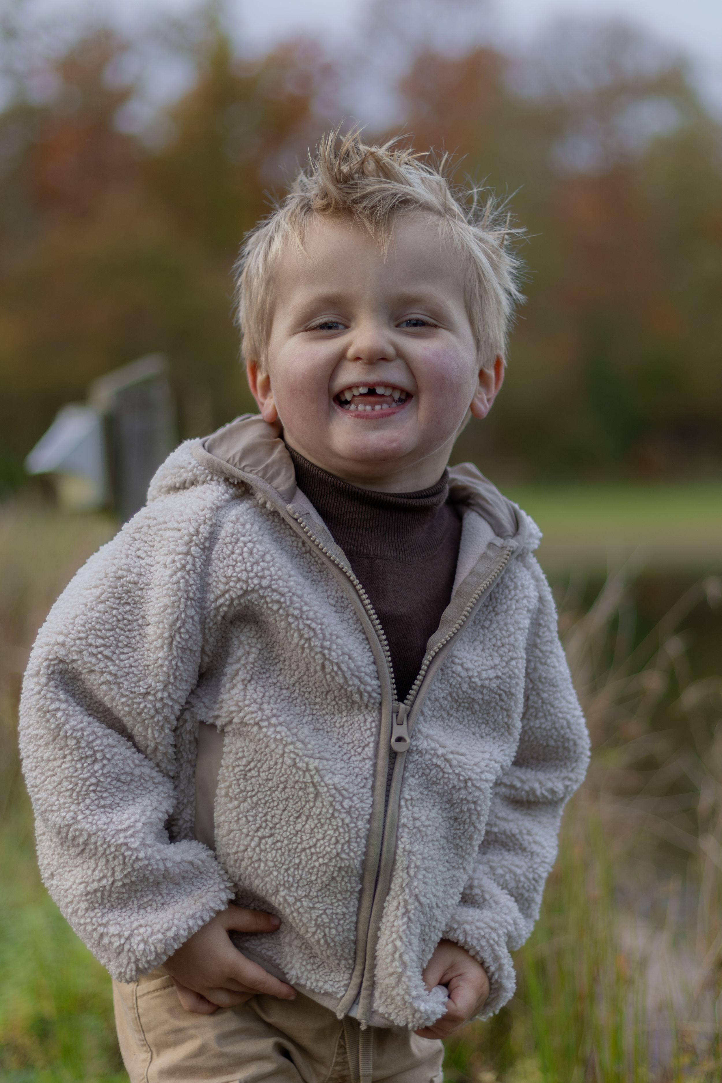 Child in cozy fleece jacket smiles happily outdoors in fall weather.