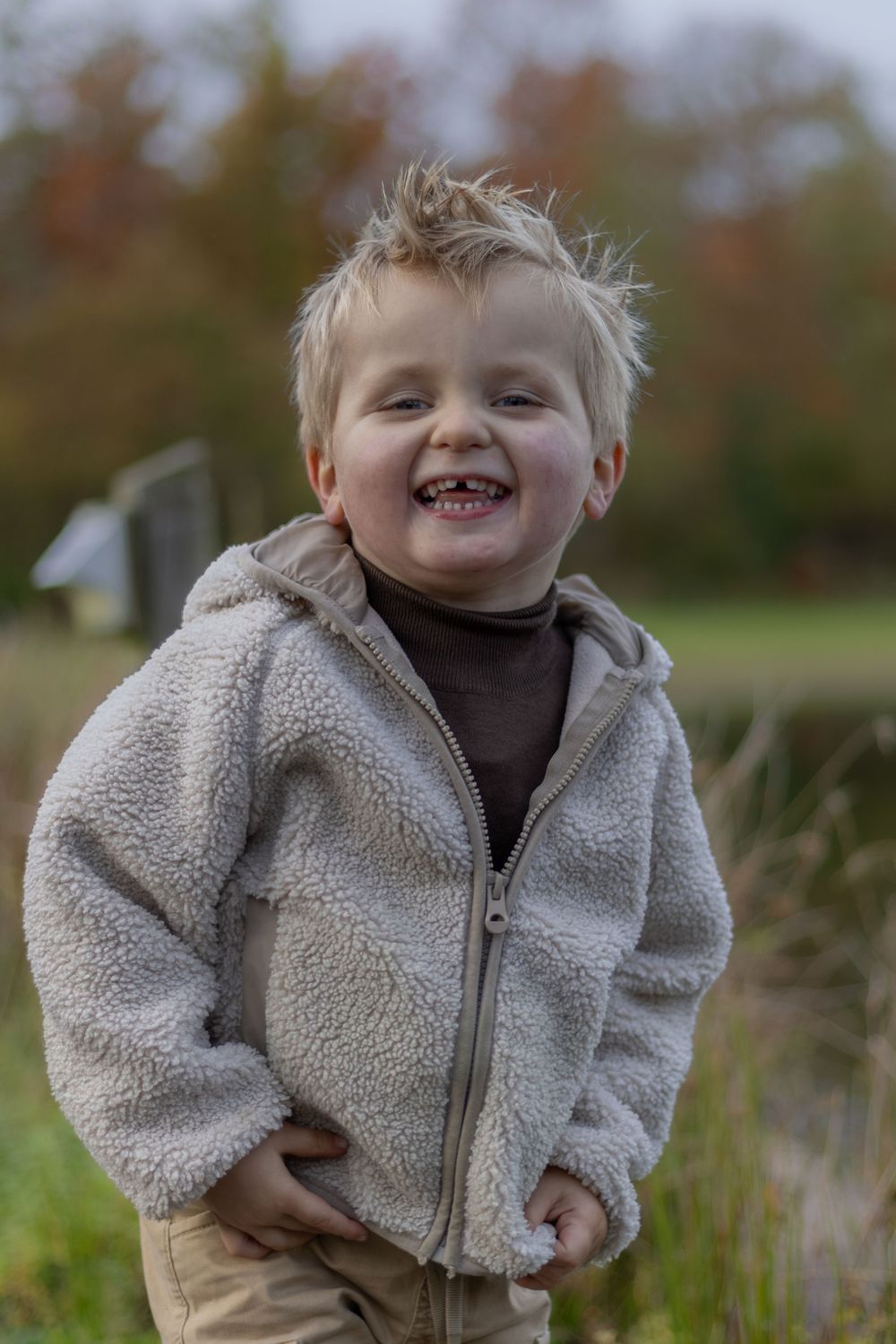 Child in cozy fleece jacket smiles happily outdoors in fall weather.