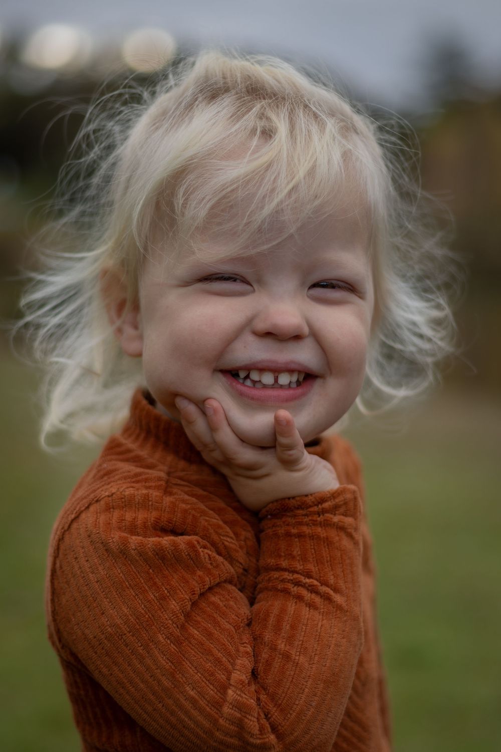 Smiling toddler in orange sweater with windswept blonde hair.