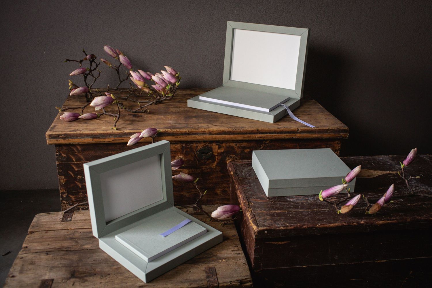 Elegant gray photo boxes arranged artistically on weathered wood with dried floral accents.