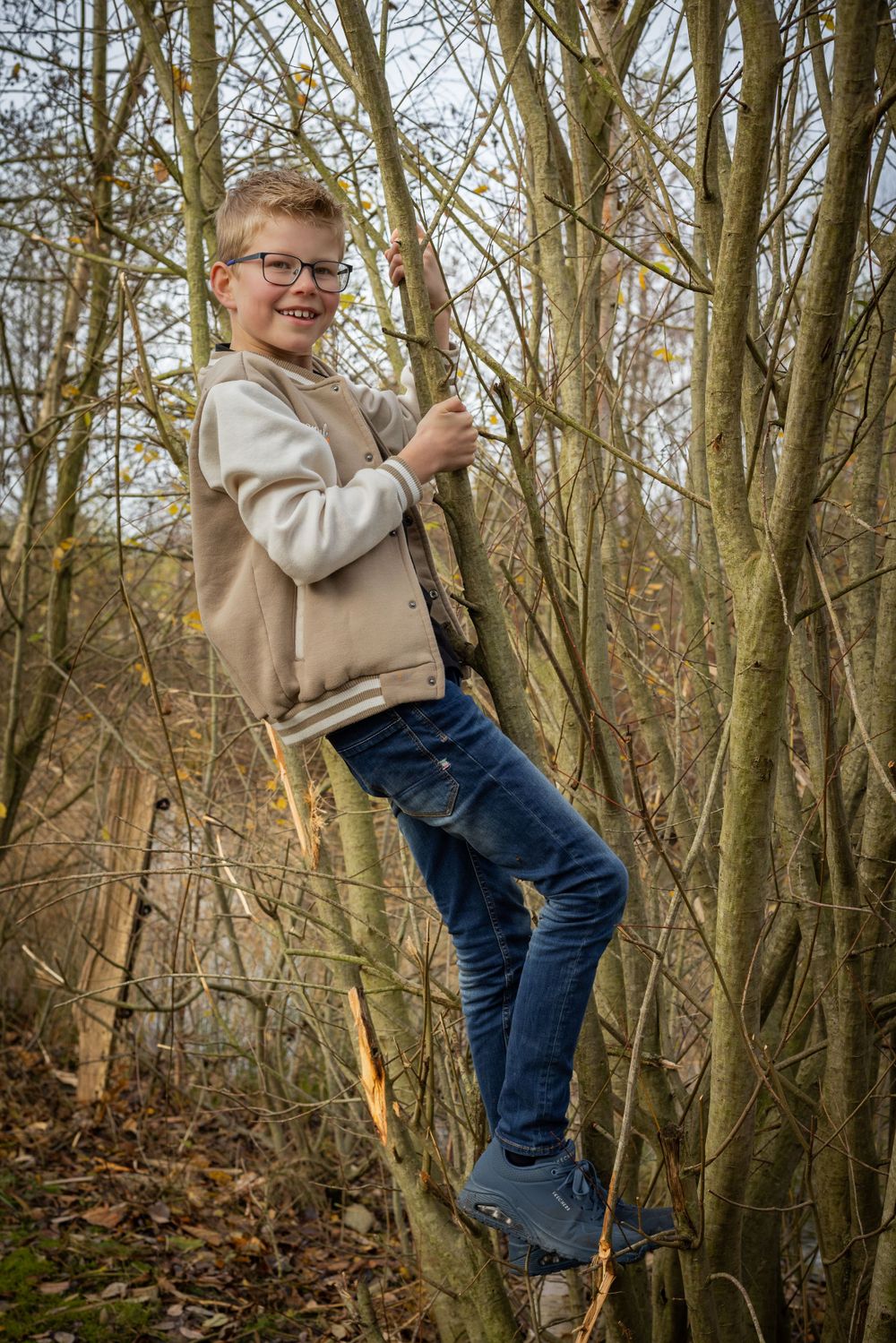 Person in beige sweater climbing trees in wooded area during autumn.