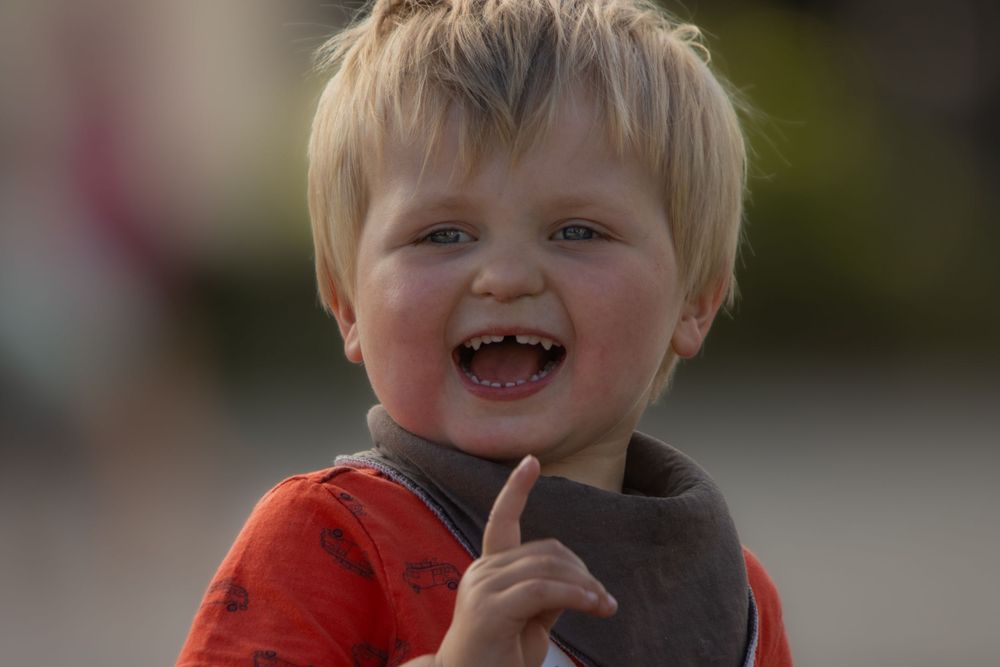 Close up portrait of toddler in red shirt smiling brightly outdoors.