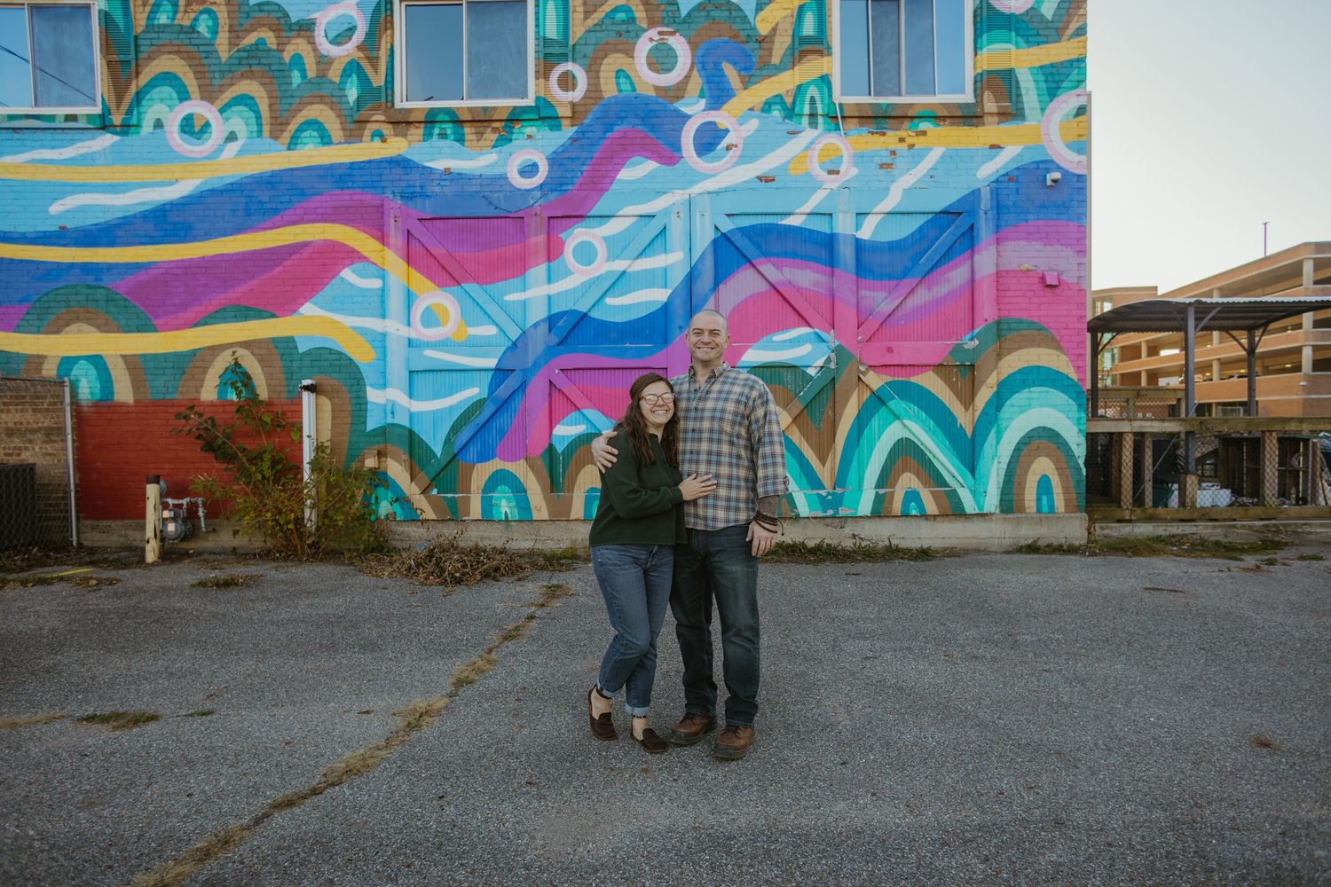 Couple standing in front of vibrant street art mural with swirling colorful designs.