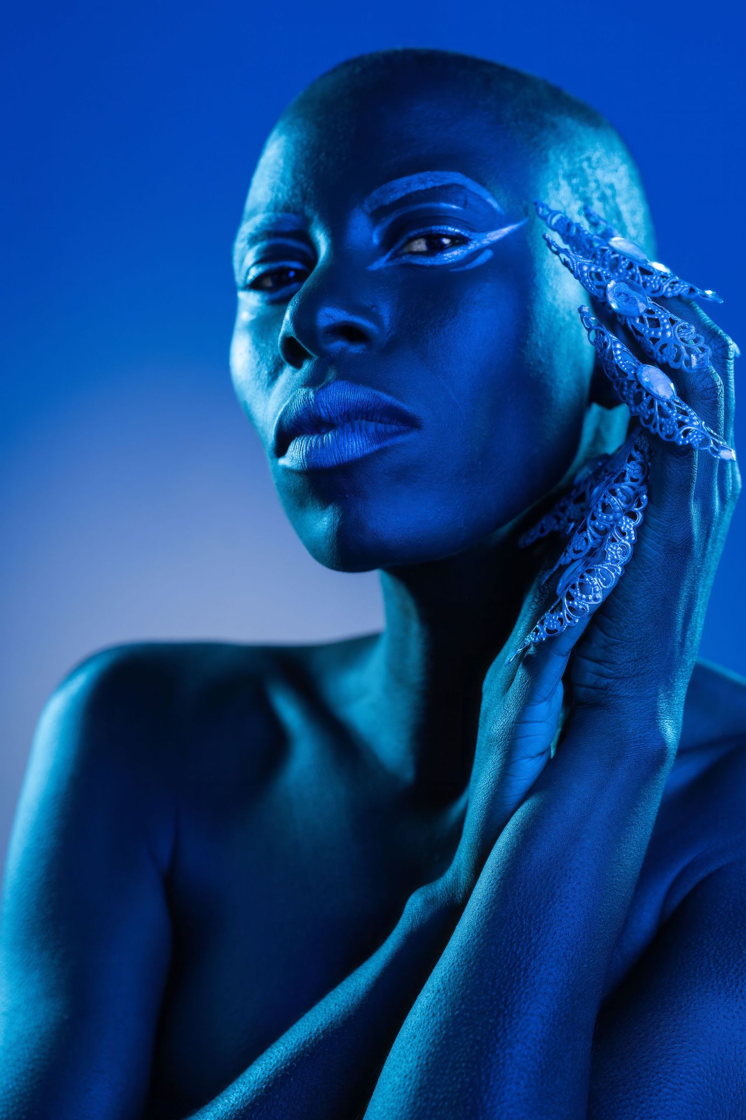 Artistic portrait with blue tonal lighting highlights striking features and dramatic shadows in a moody studio composition.