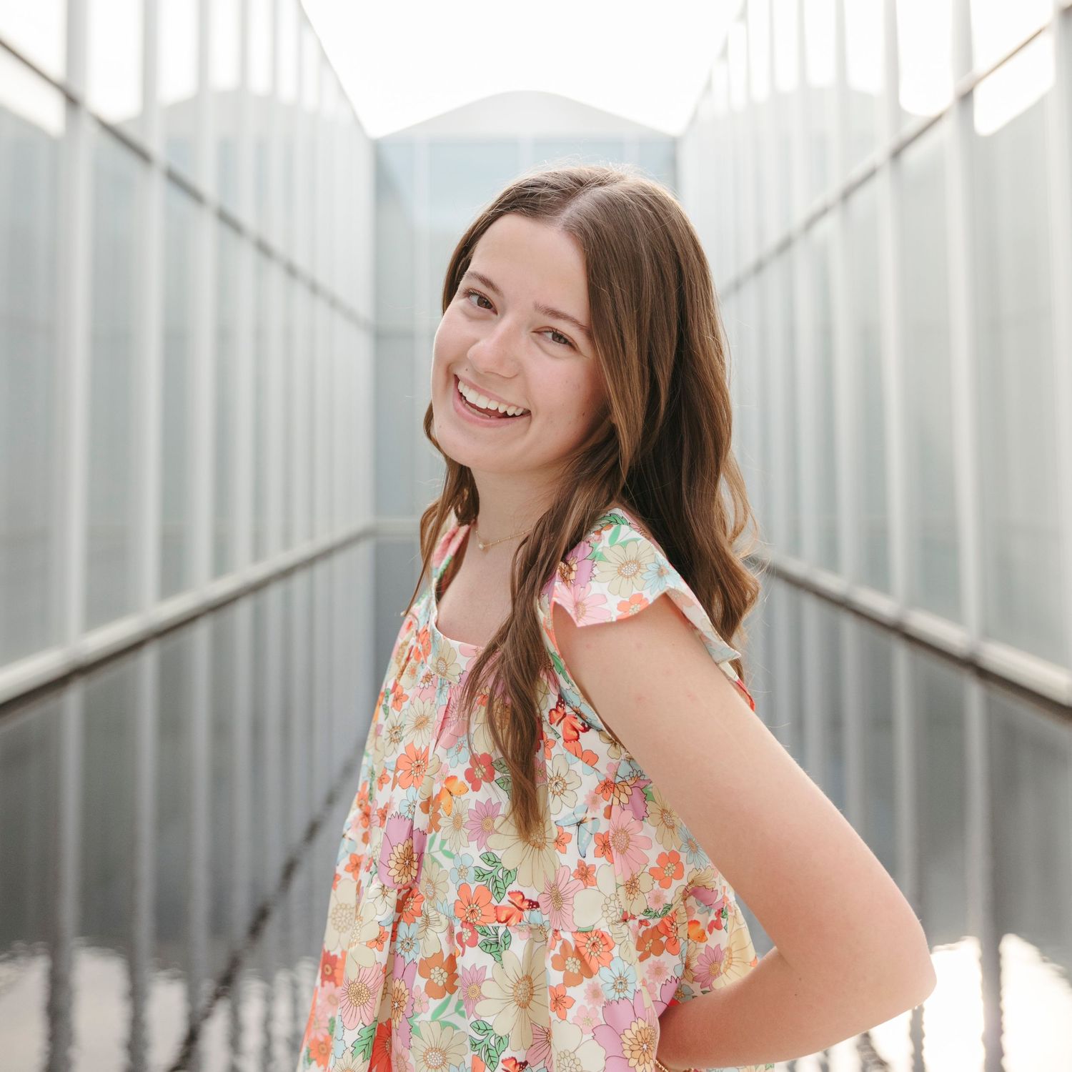 Bright outdoor portraits with person in floral dress posing against metal architectural elements.