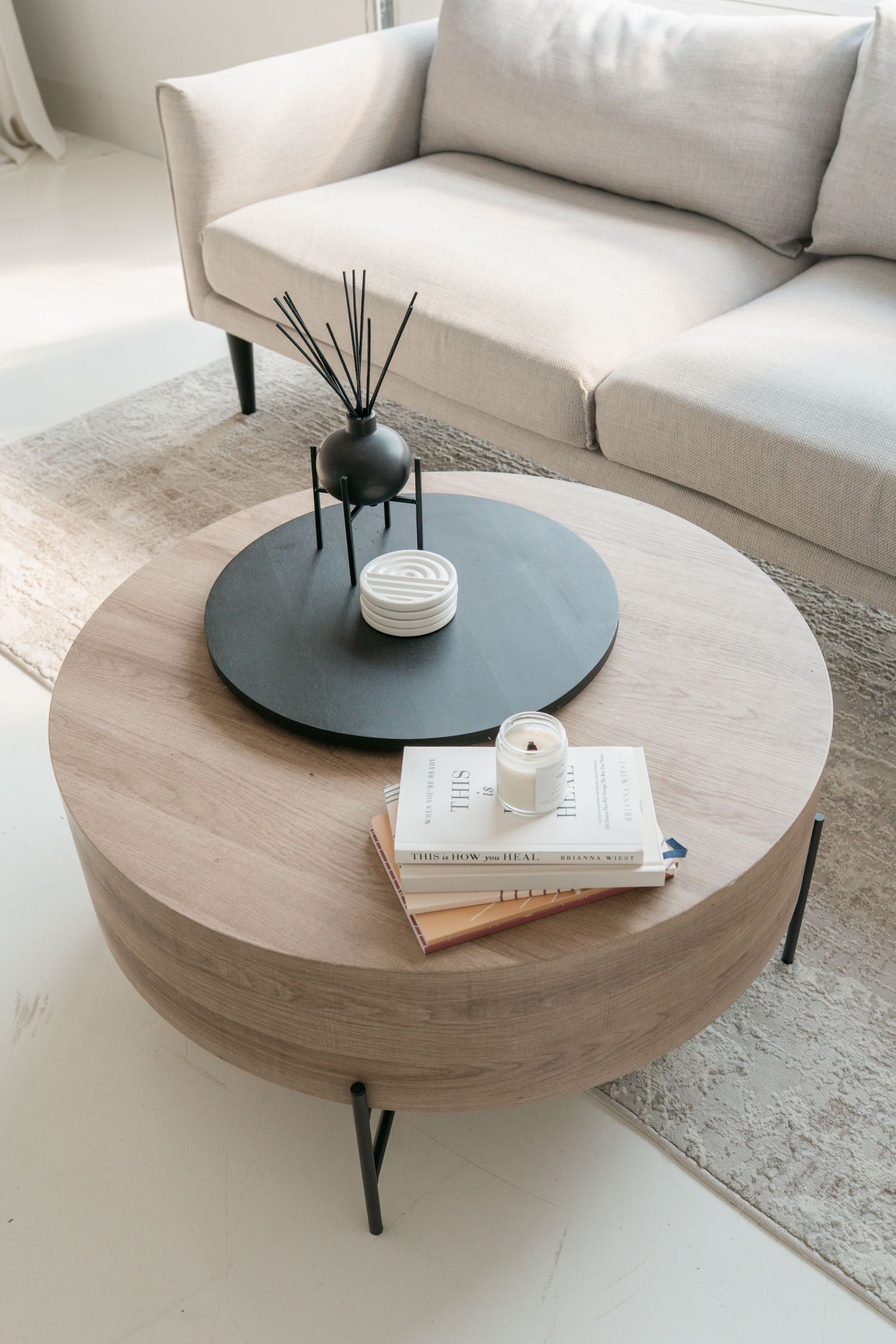 Modern circular coffee table with natural wood top and black legs styled with books and decor on a light carpet.