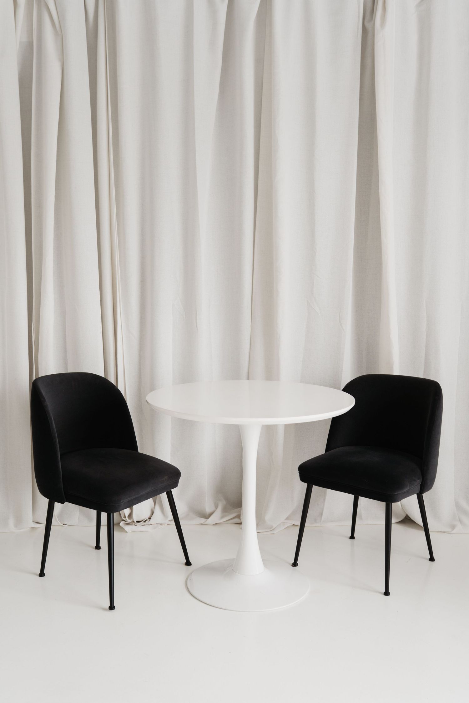 White fabric curtains cascading in gentle folds against a bright wall with dark furniture silhouettes below.