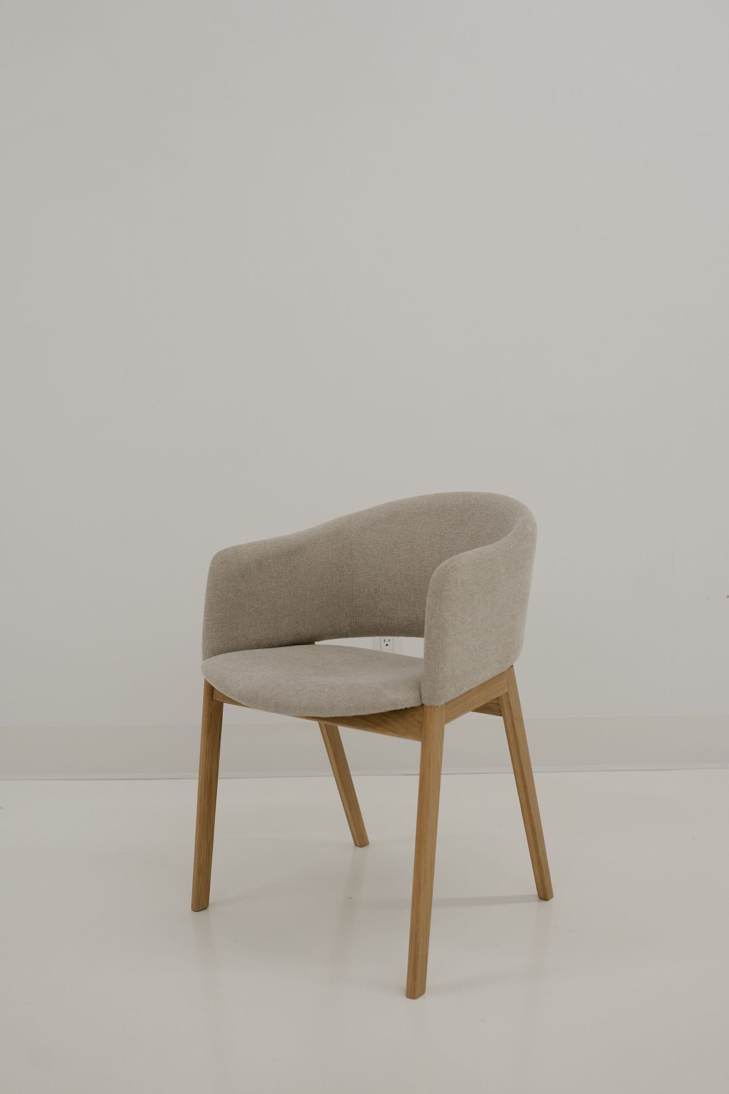 Modern dining chair with beige upholstered curved back, wooden legs and minimalist Scandinavian design against white background.