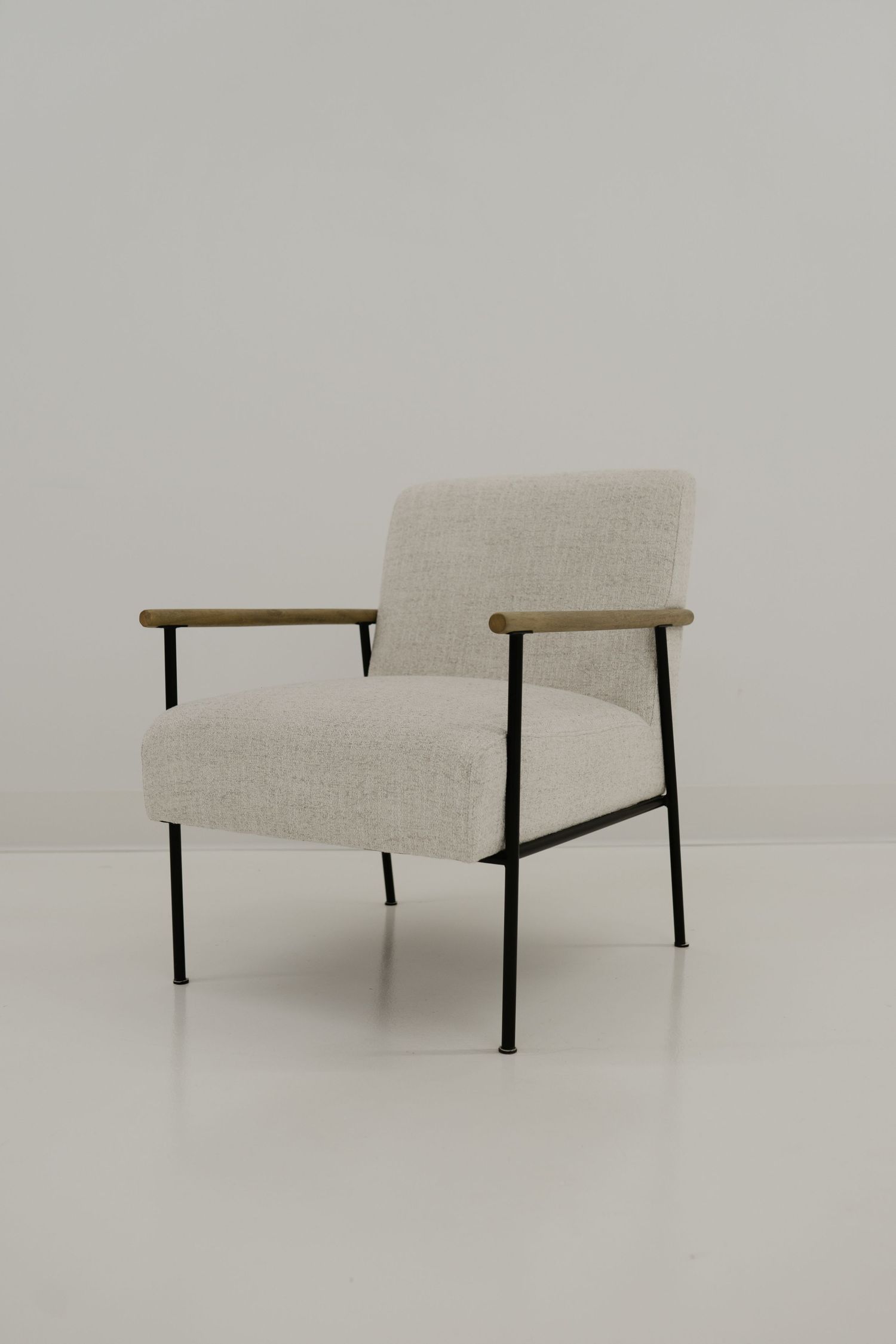 A minimalist armchair with beige upholstery, black metal frame, and wooden armrests sits against a light gray background.