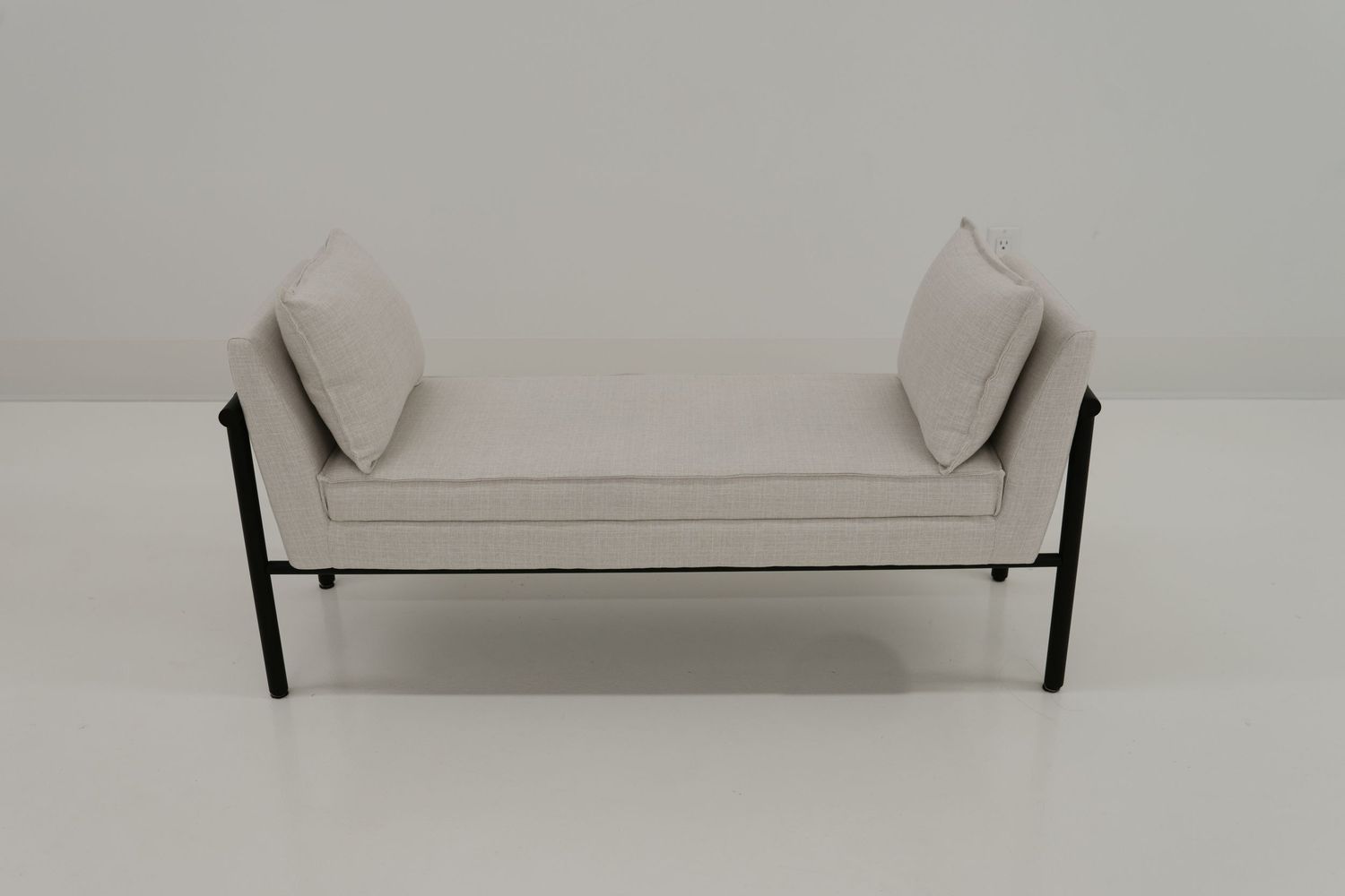 Minimalist daybed with light gray upholstery and black metal frame features two bolster pillows on opposite ends.