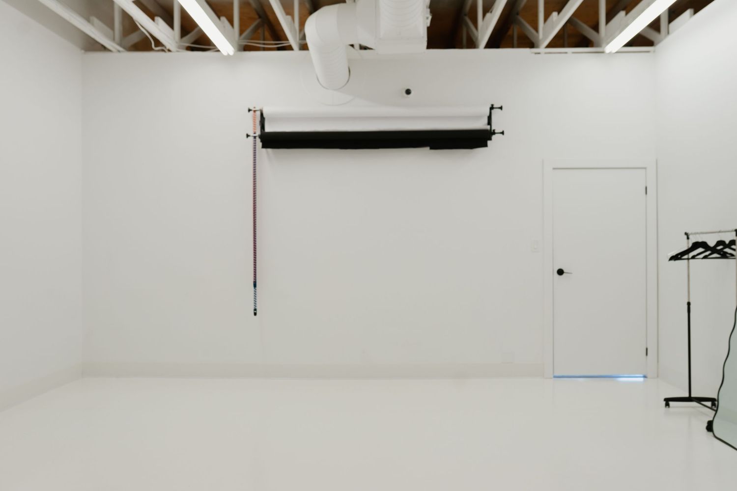 White photography studio interior with exposed wooden beams and a black light fixture mounted on the wall.