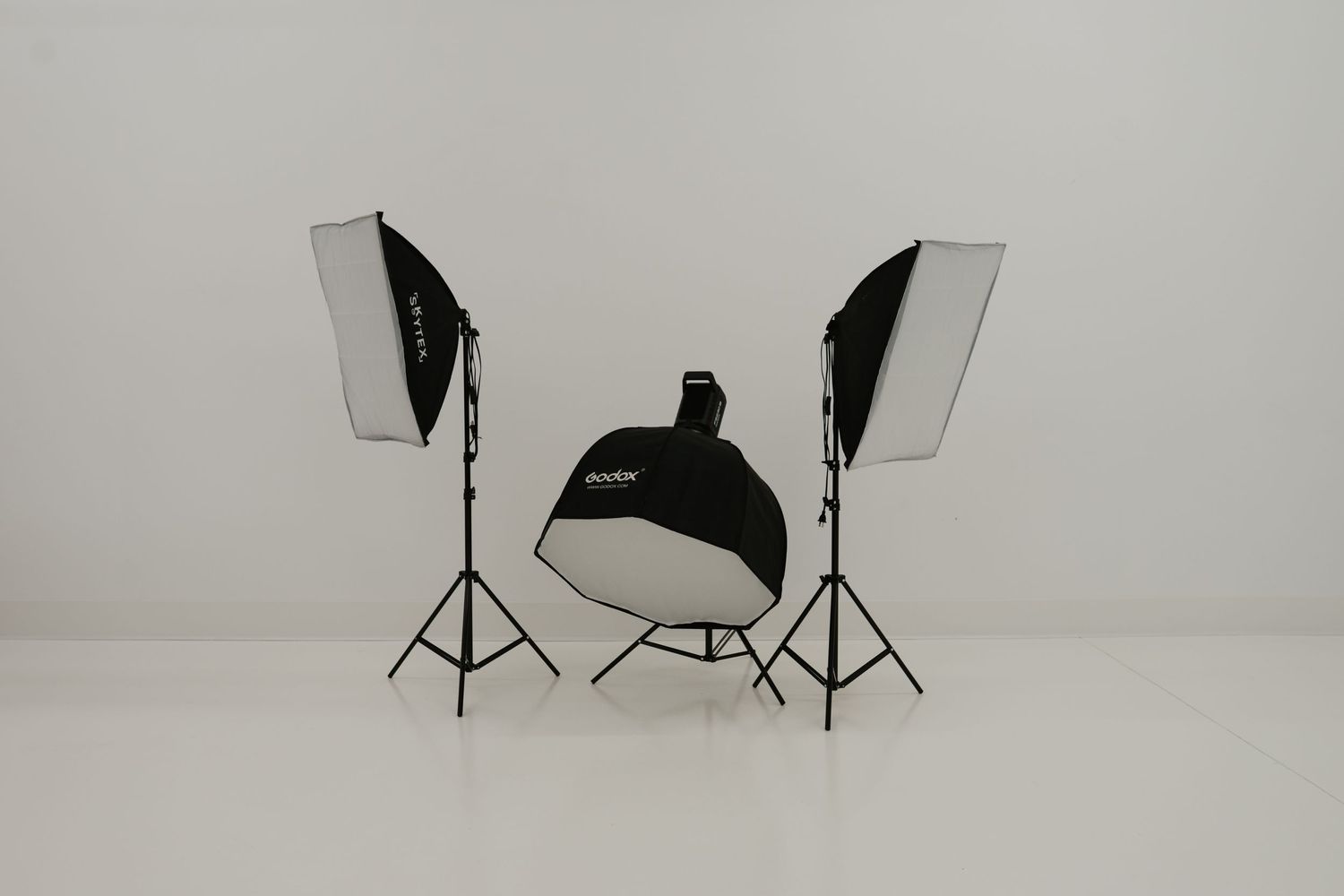 Professional photography studio setup with two softboxes and reflector on white seamless background.