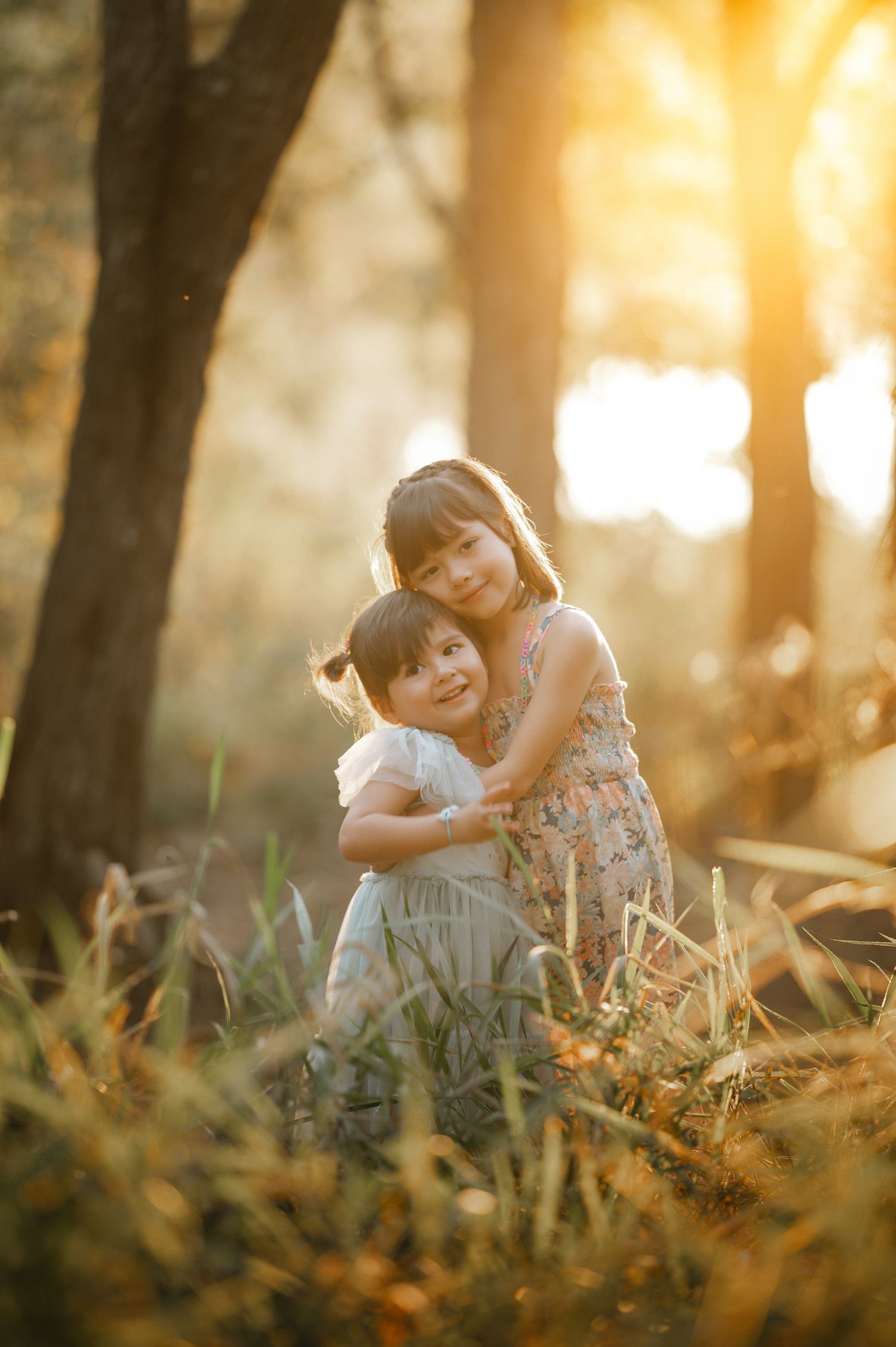 Children embracing in field during golden hour with trees in background.