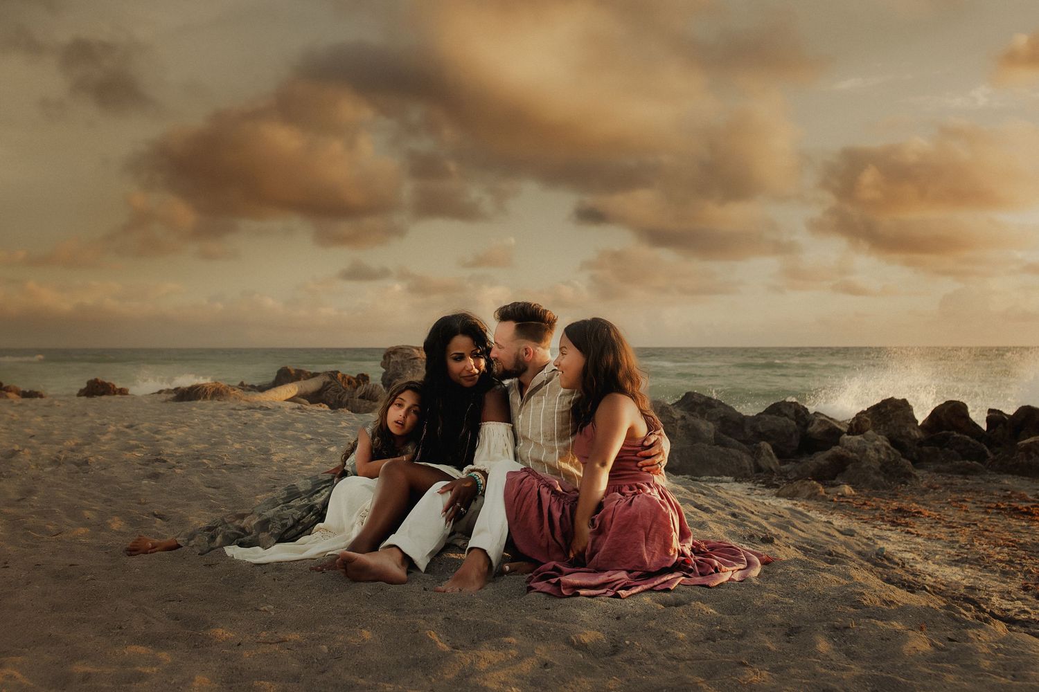 People sitting together on a beach with rocks at sunset, creating a warm atmospheric mood.