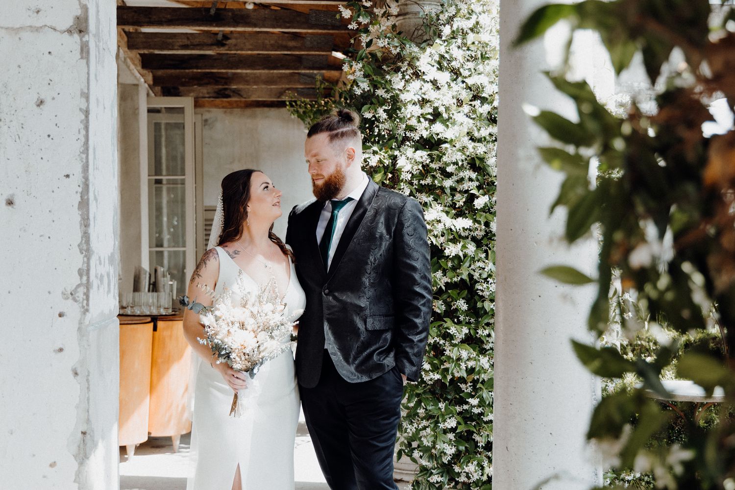 A bride and groom pose together in an elegant outdoor garden setting, captured by Apertured Media Auckland Wedding Photographer.