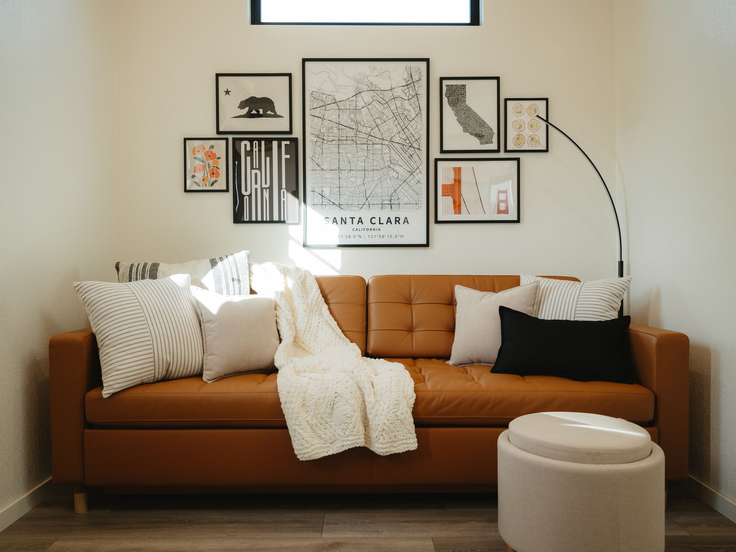 A modern living room features a brown leather couch with California-themed wall art and throw pillows.