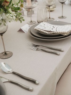 Elegant table setting with white flowers, wine glasses, and silver cutlery on a neutral tablecloth.