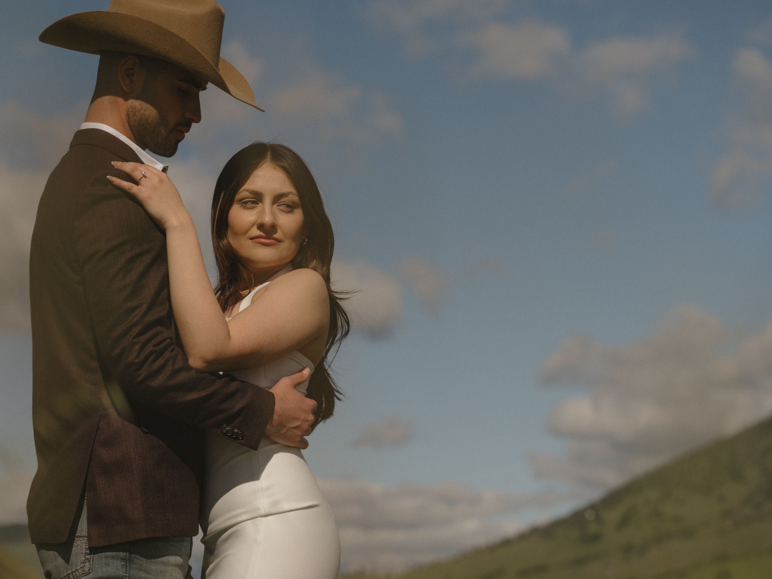A romantic couple embraces in warm sunlight against a rural backdrop with a cowboy hat silhouette.