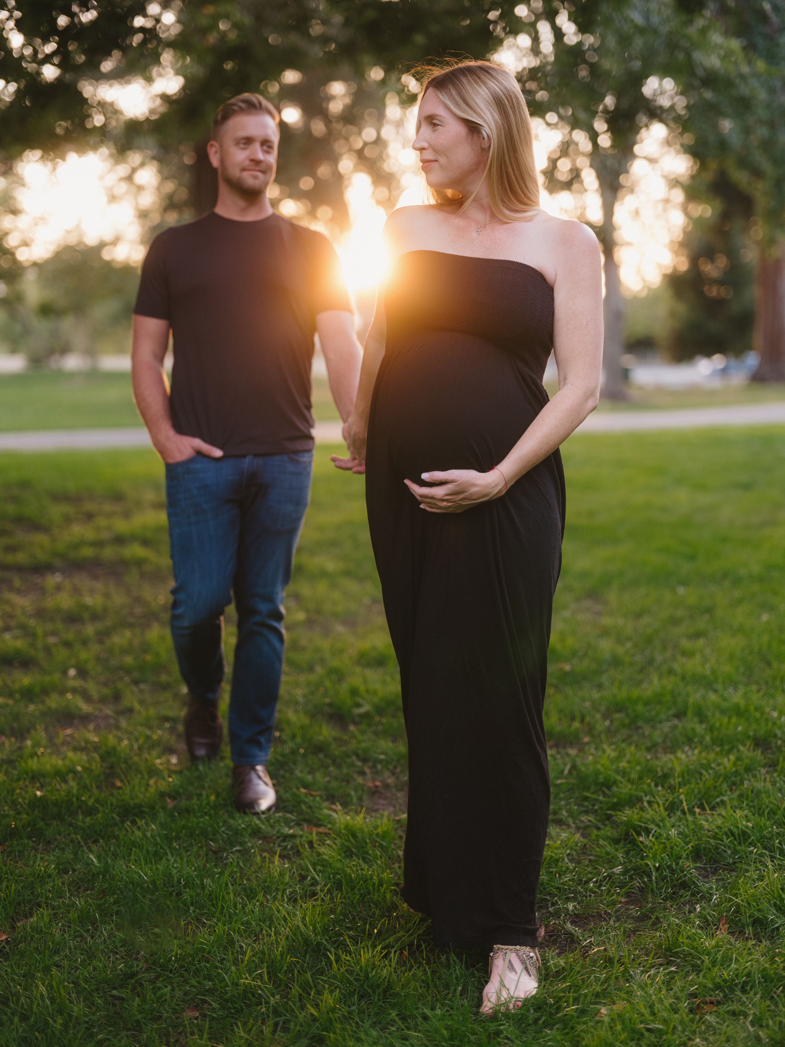 A maternity photo captures an expectant couple in sunset lighting on a grassy lawn.