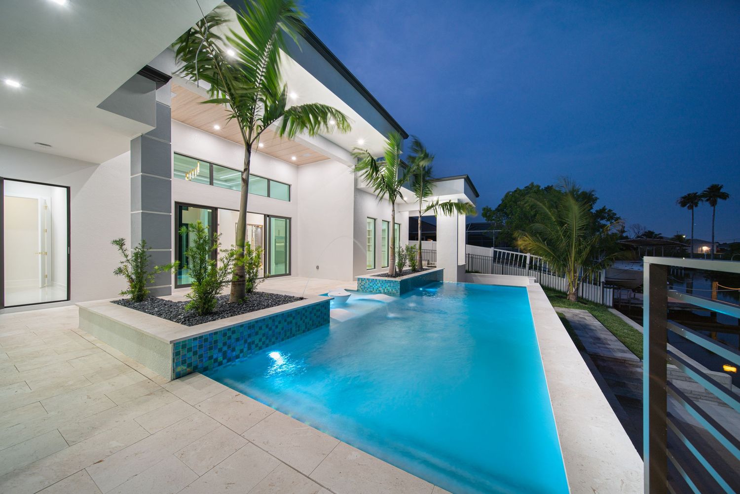 Modern gray and black contemporary house with glass garage doors and manicured lawn on concrete driveway.