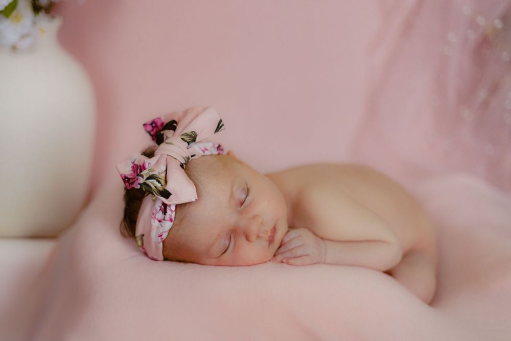 Pink baby headband with delicate bow adorns sleeping newborn on soft blanket in dreamy nursery setting.