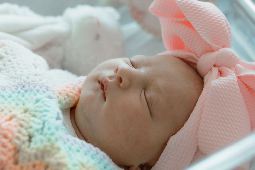 Peaceful sleeping infant wrapped in colorful knitted blanket and pink cap.