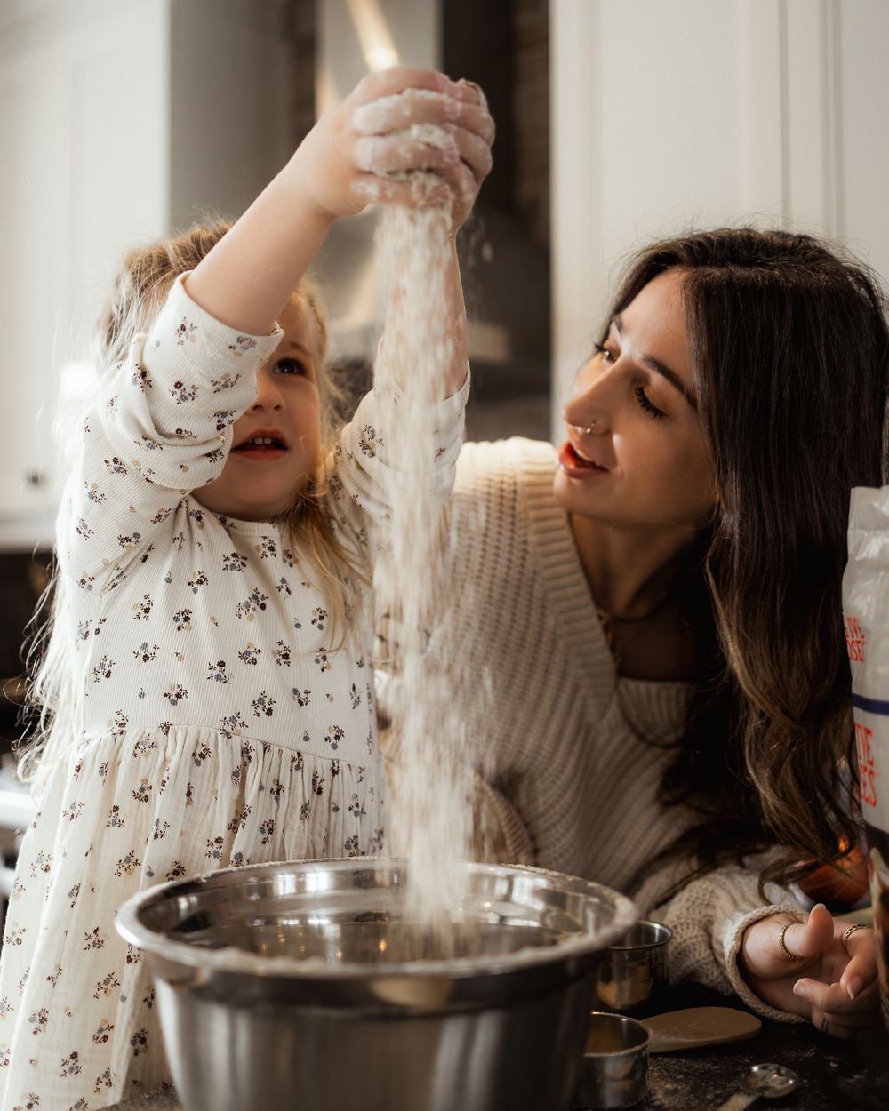 A child and adult baking together in a kitchen, playfully sprinkling flour while making dough.